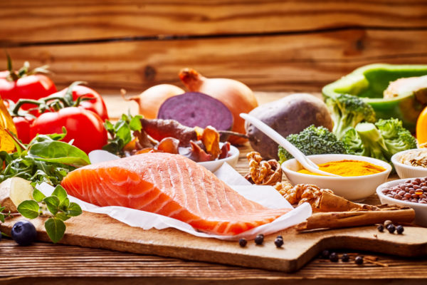 Healthy fresh raw food for the heart in a banner format on rustic wood with salmon, assorted spices, herbs, nuts, peppers, blueberries, tomato, onion, broccoli, garlic, soy sauce and olive oil
